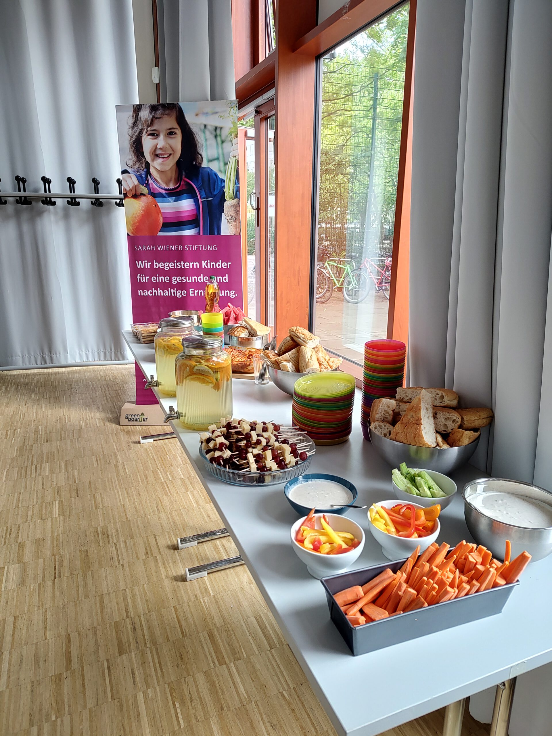 Ein aufgebautes Buffet im Vordergrund rechts. Dahinter das Banner der Sarah Wiener Stiftung